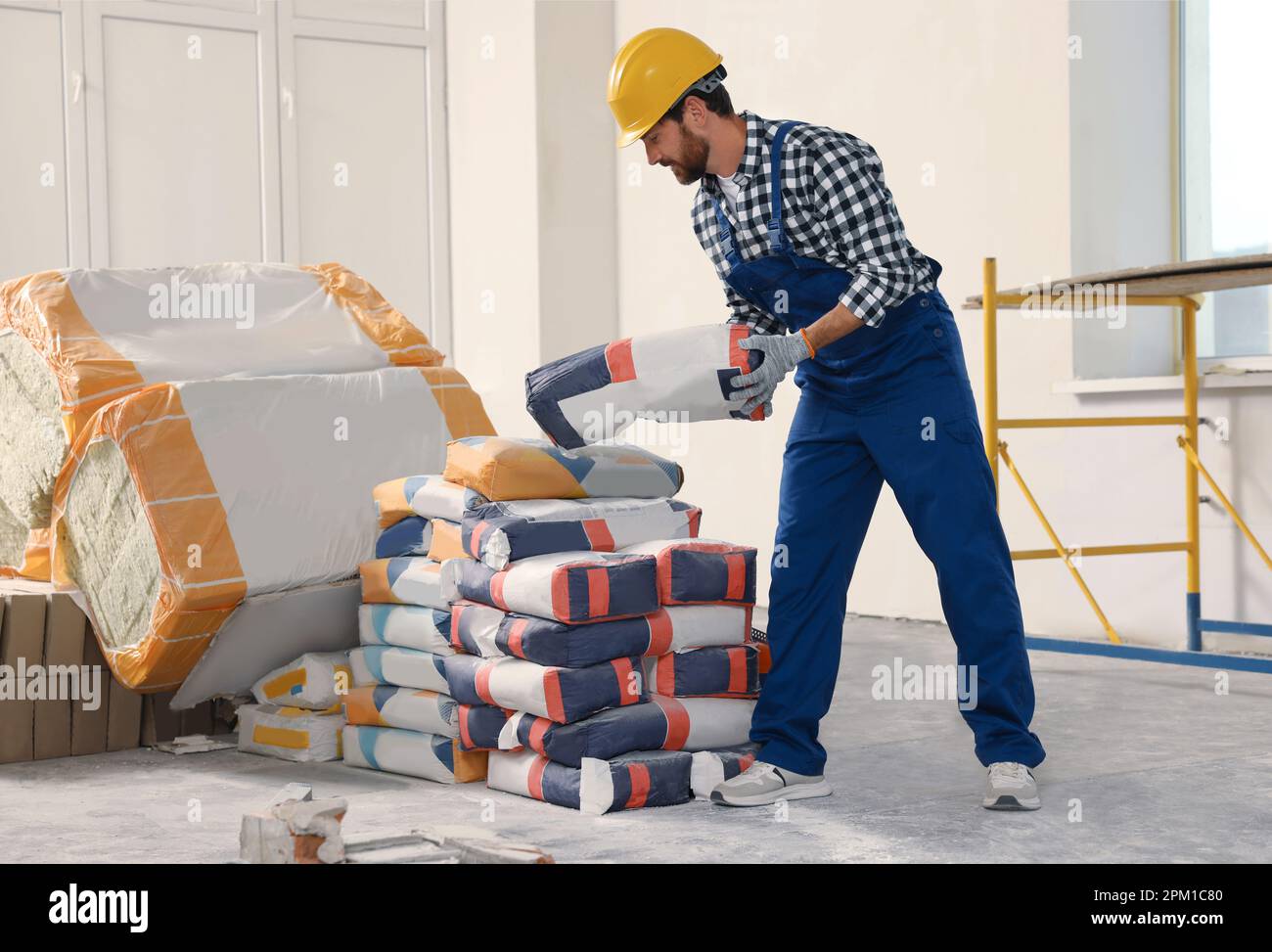 Professional builder in uniform with bag of cement indoors Stock Photo