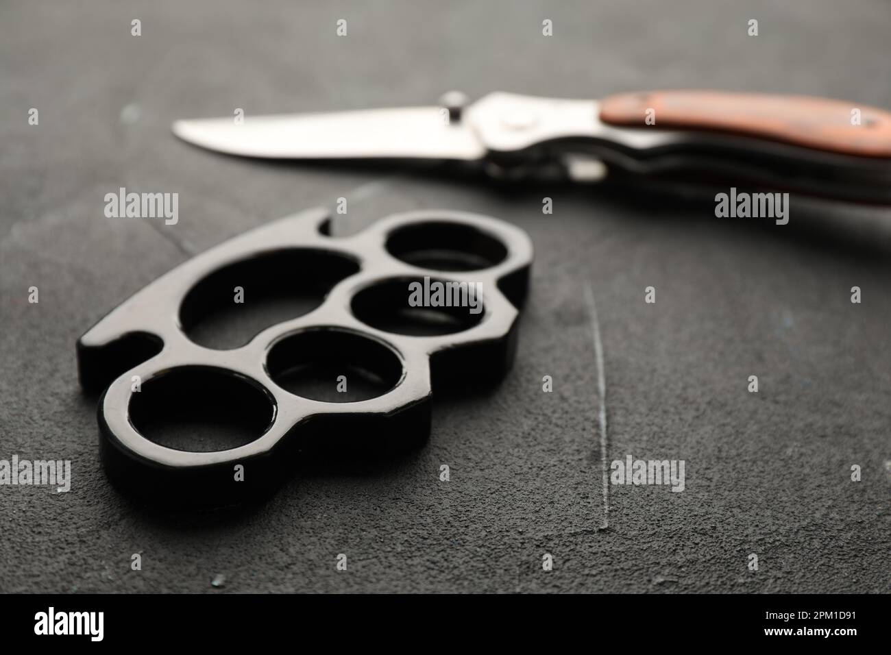 https://c8.alamy.com/comp/2PM1D91/brass-knuckles-and-knife-on-black-stone-background-closeup-2PM1D91.jpg