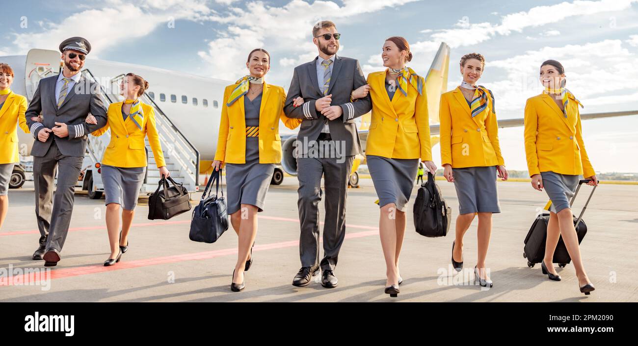 Cheerful aircrew with travel bags walking under cloudy sky Stock Photo