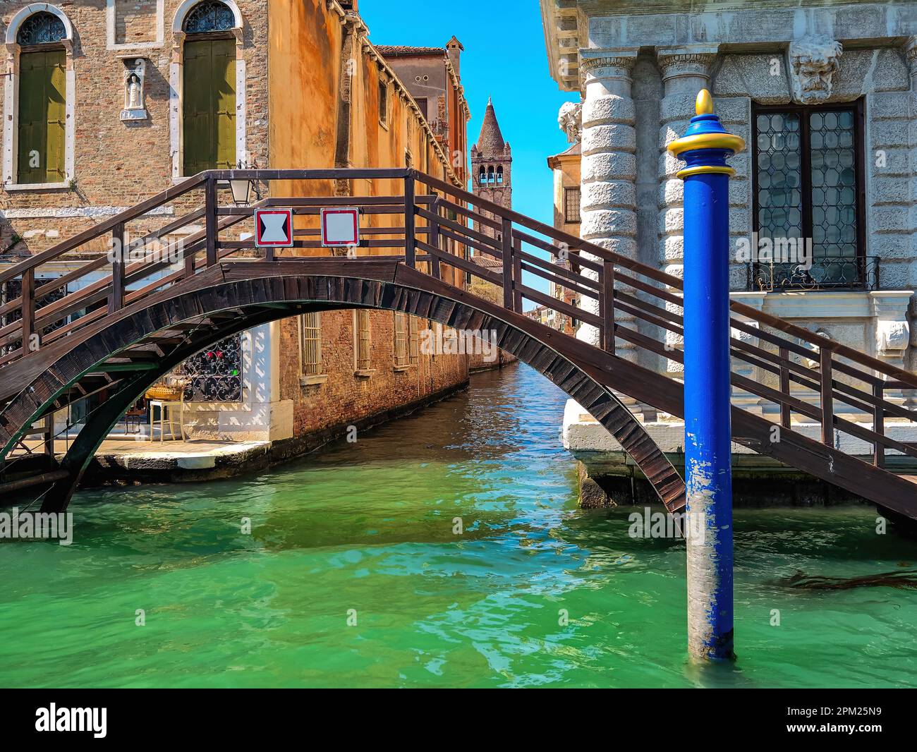 Blue pillar and small wooden bridge over the canal with beautiful green water in Venice, Italy. Stock Photo