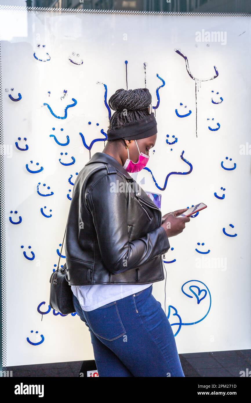 Young black woman wearing a sanitary mask and consulting her phone, in  front of the tagged panel of a bus shelter. Brussels Stock Photo - Alamy