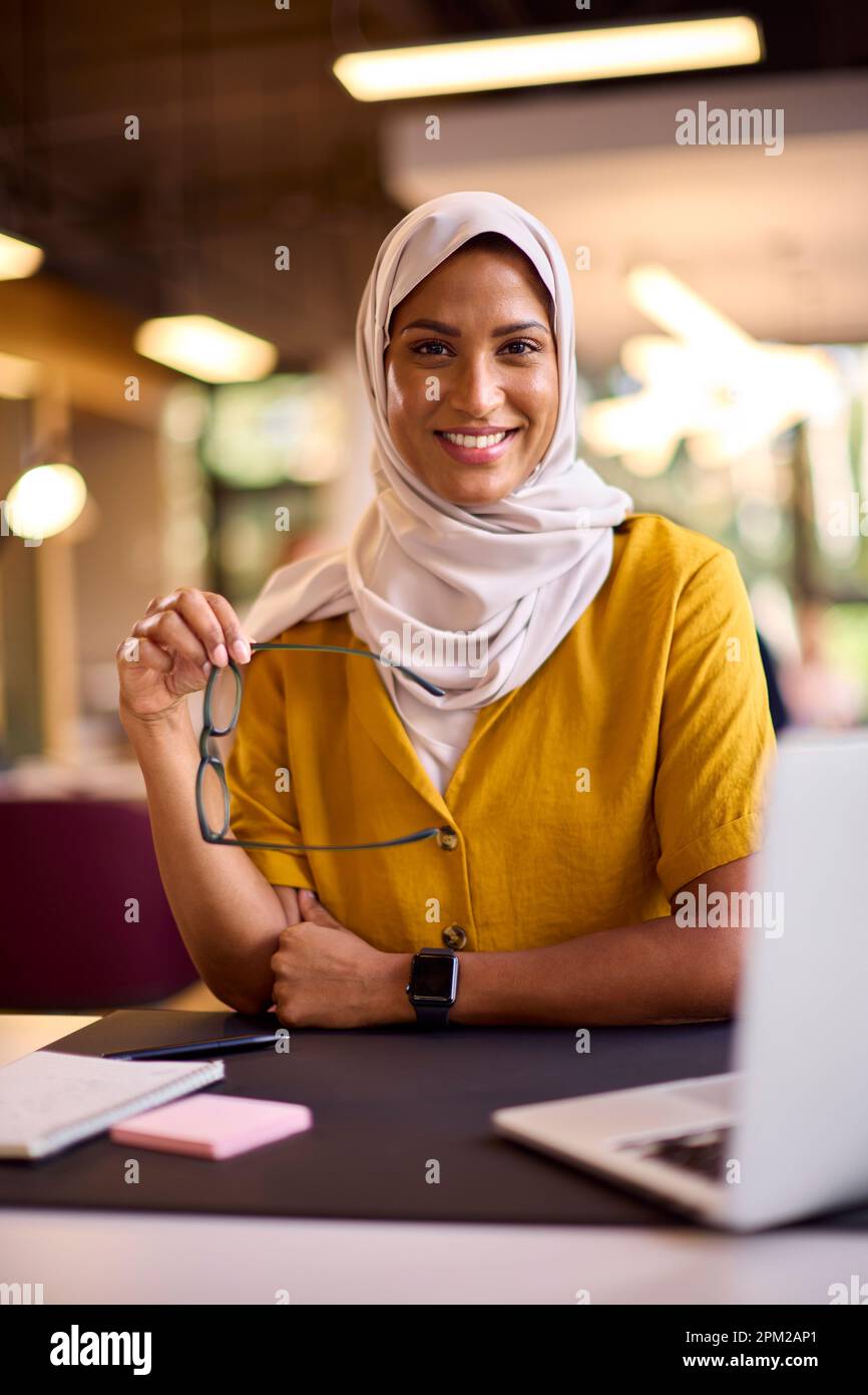 Portrait Of Mature Businesswoman Wearing Headscarf Working On Laptop At Desk In Office Stock Photo