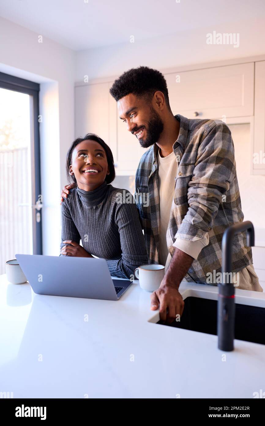 Young Couple At Home Looking At Laptop On Counter In Kitchen Together Stock Photo