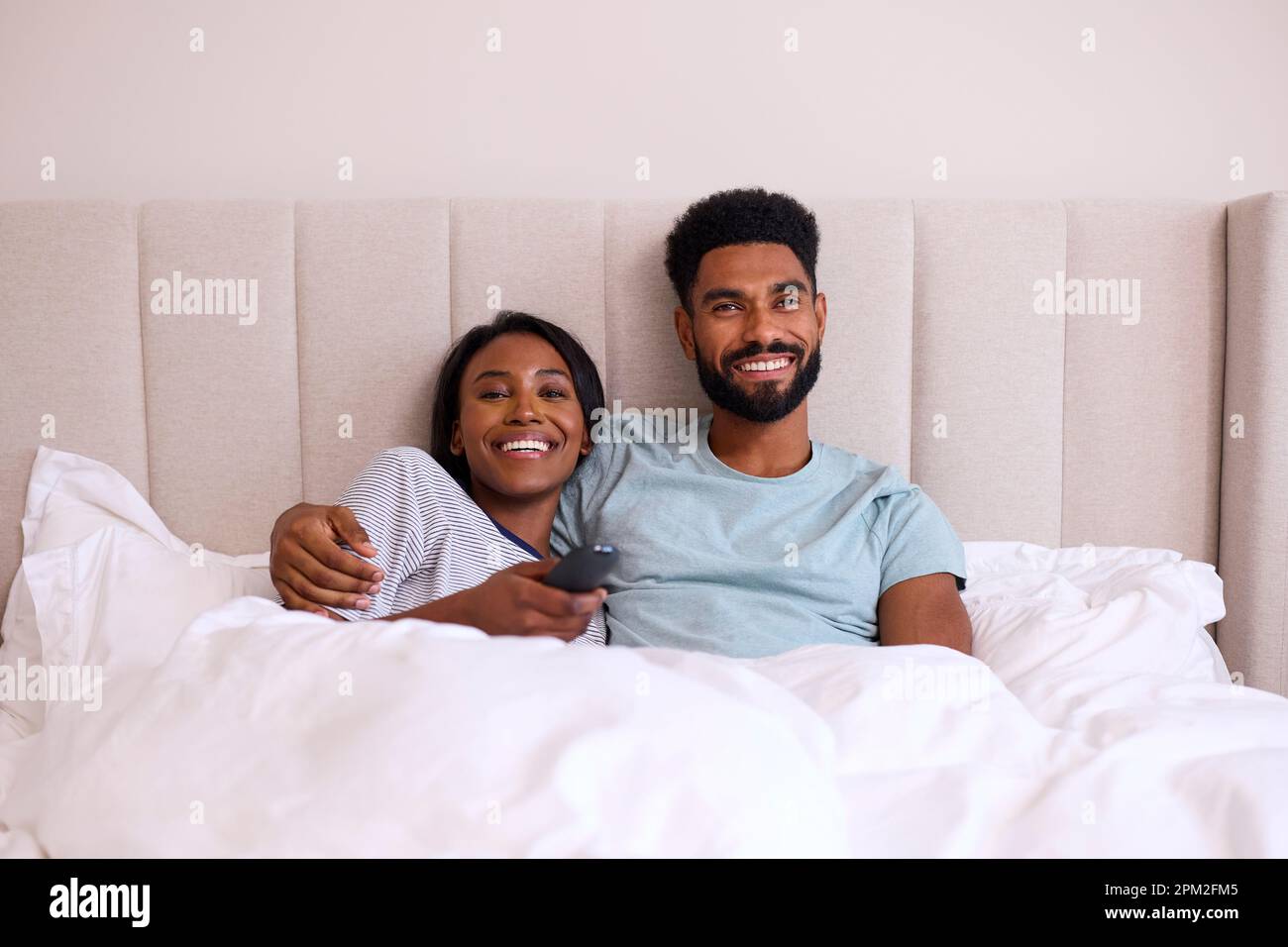 Loving Young Couple At Home Watching TV In Bed Together Stock Photo