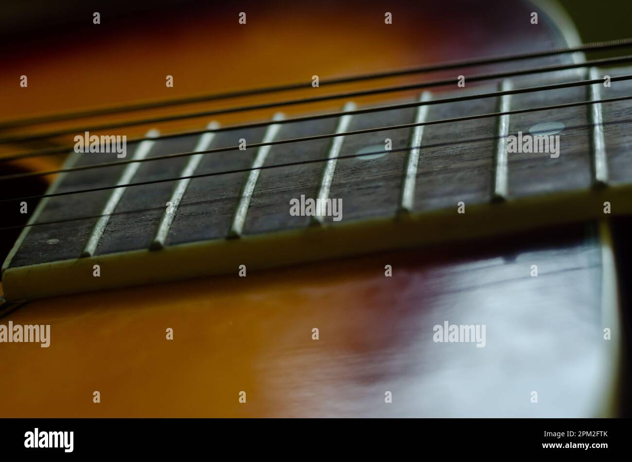 A close-up image of an acoustic guitar with a sharp focus on the fretboard and strings Stock Photo