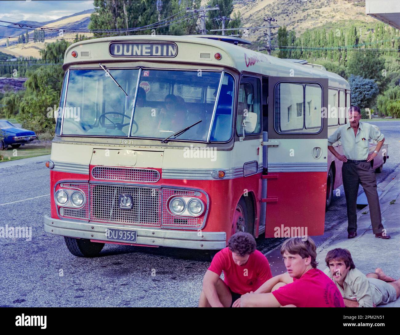 A 1981 historic image of a Railways Road Services Bedford SB3 Cruiser Coach stopped beside the road on its journey to Dunedin from Christchurch on the south island of New Zealand. Passengers can be seen sitting and standing near the bus while they wait for the driver. Stock Photo