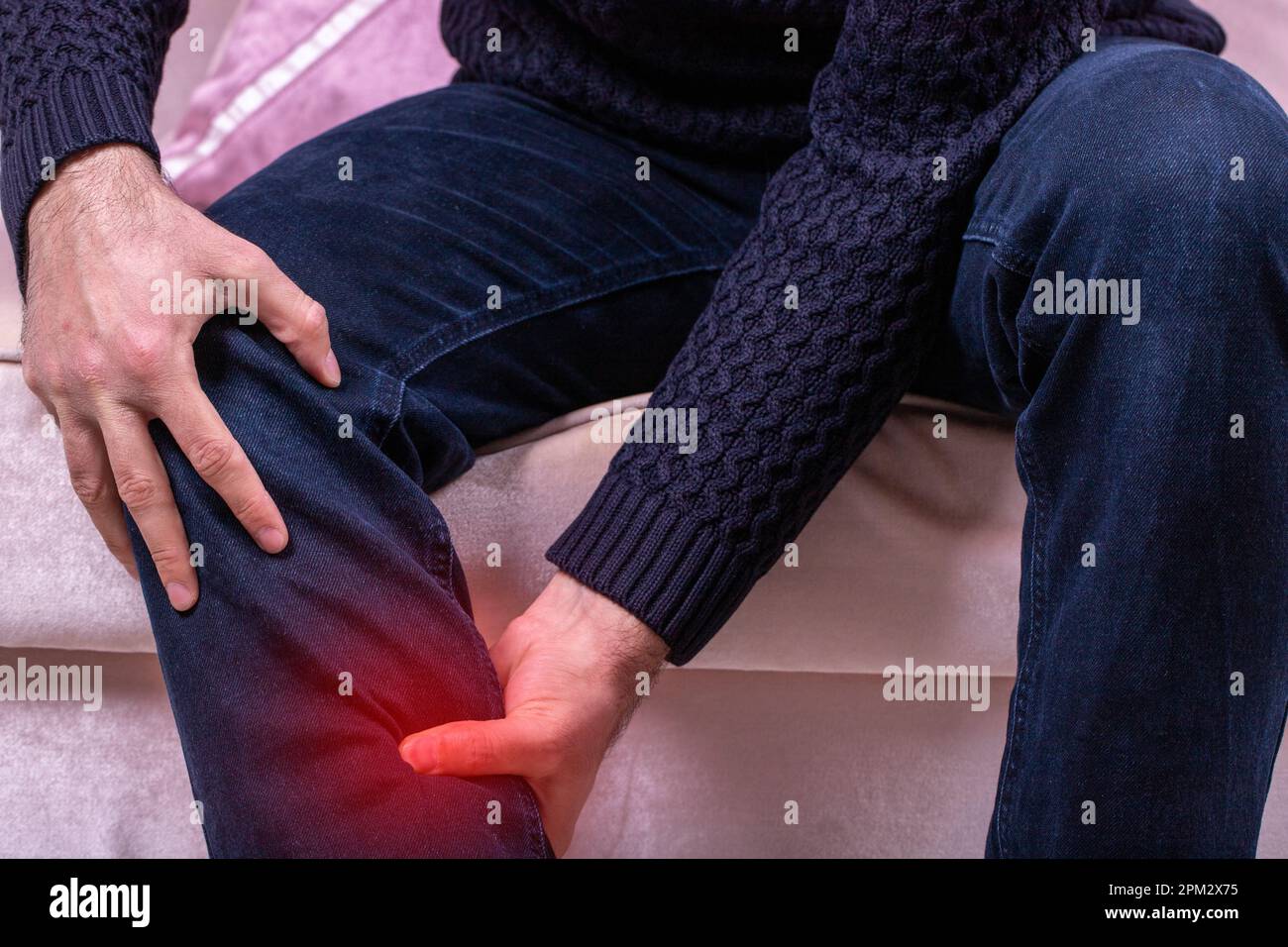 Man with leg calf pain. The man's calf muscle cramped, massage of male leg at home, painful area highlighted in red Stock Photo