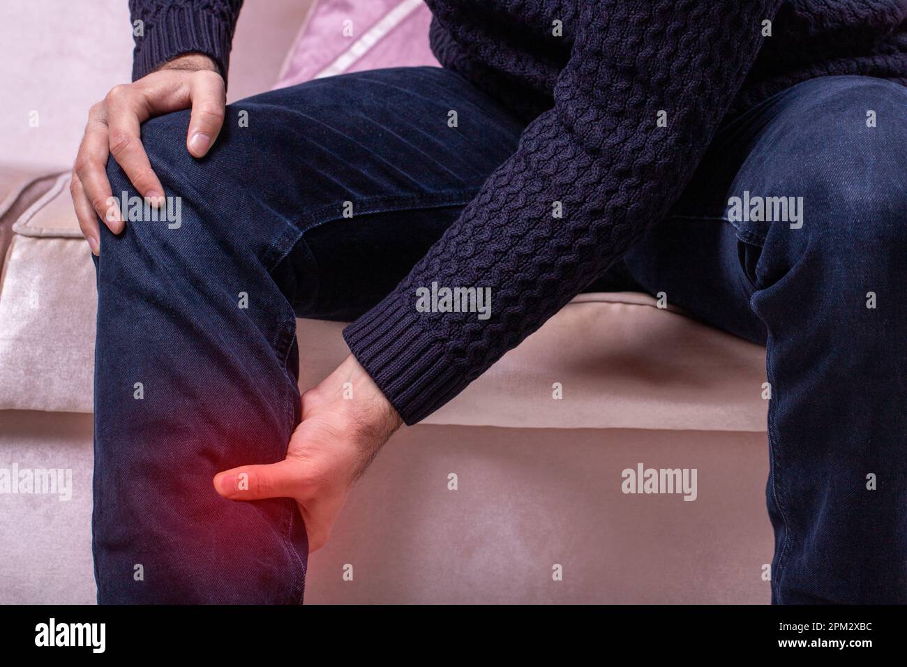 Man with leg calf pain. The man's calf muscle cramped, massage of male leg at home, painful area highlighted in red Stock Photo