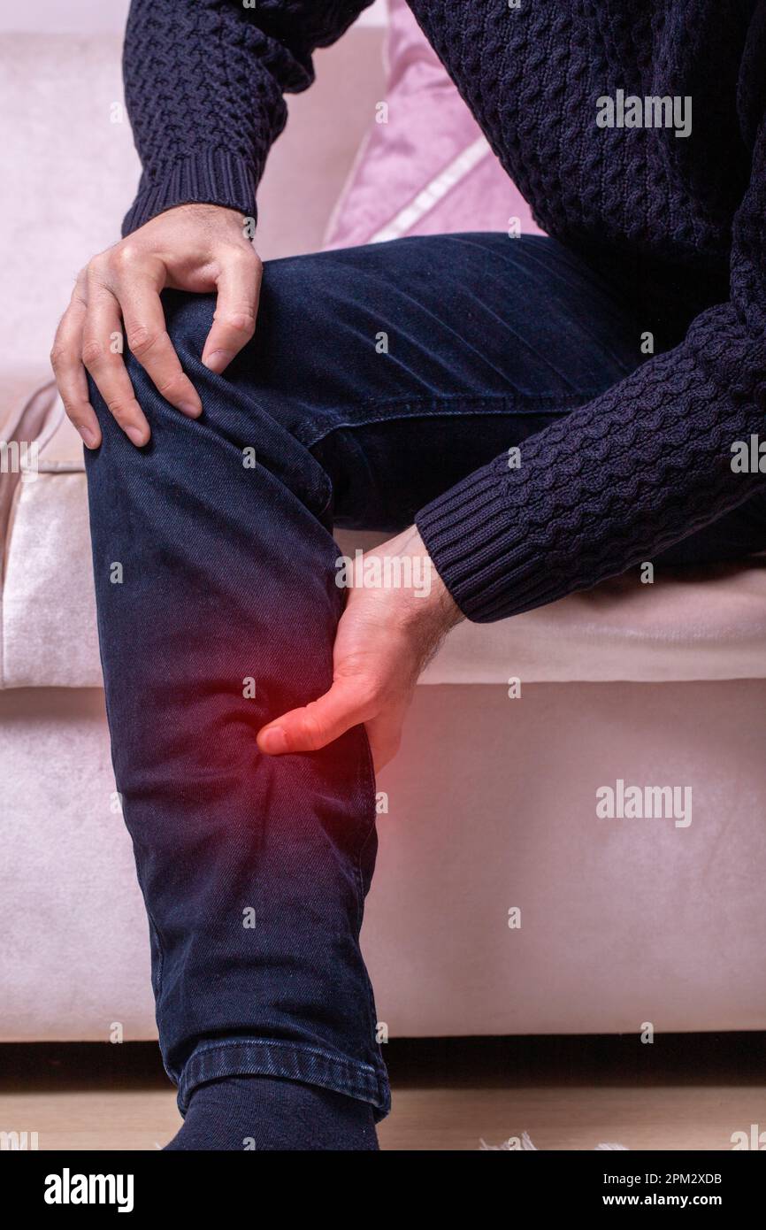 Man with leg calf pain. The man's calf muscle cramped, massage of male leg at home, painful area highlighted in red Stock Photo