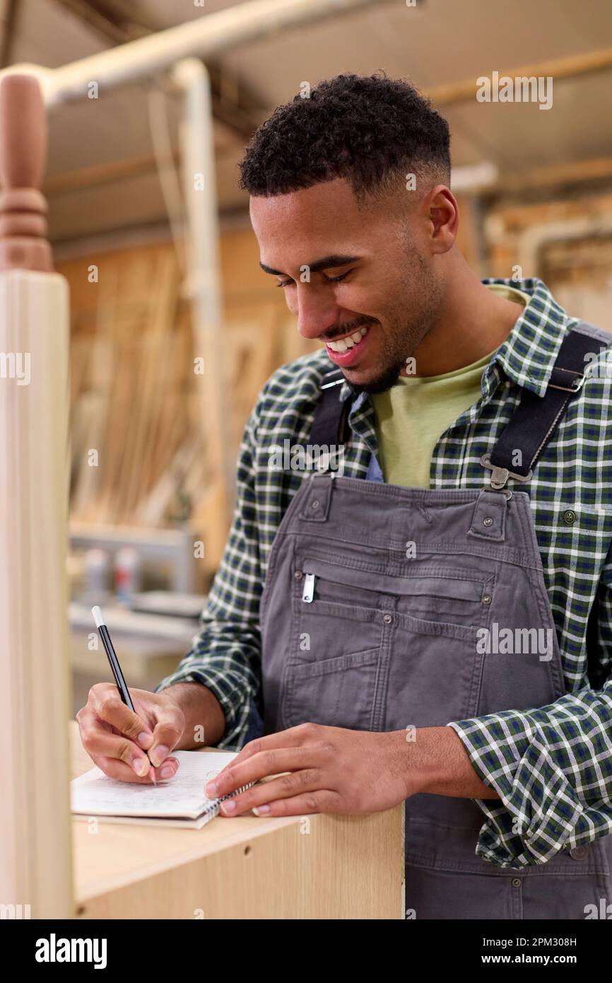 Male Apprentice Working As Carpenter In Furniture Workshop Making Notes Stock Photo