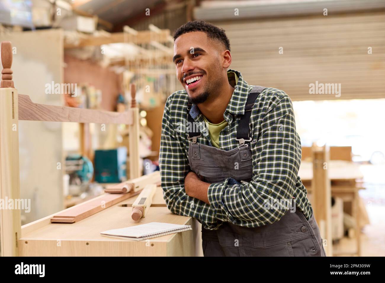 Portrait Of Male Apprentice Working As Carpenter In Furniture Workshop ...