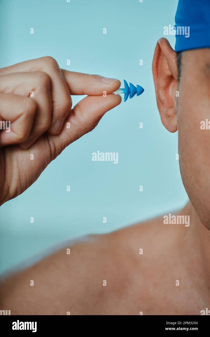 a swimmer man, wearing a blue swimming cap, puts an earplug in his ear, in a swimming pool Stock Photo