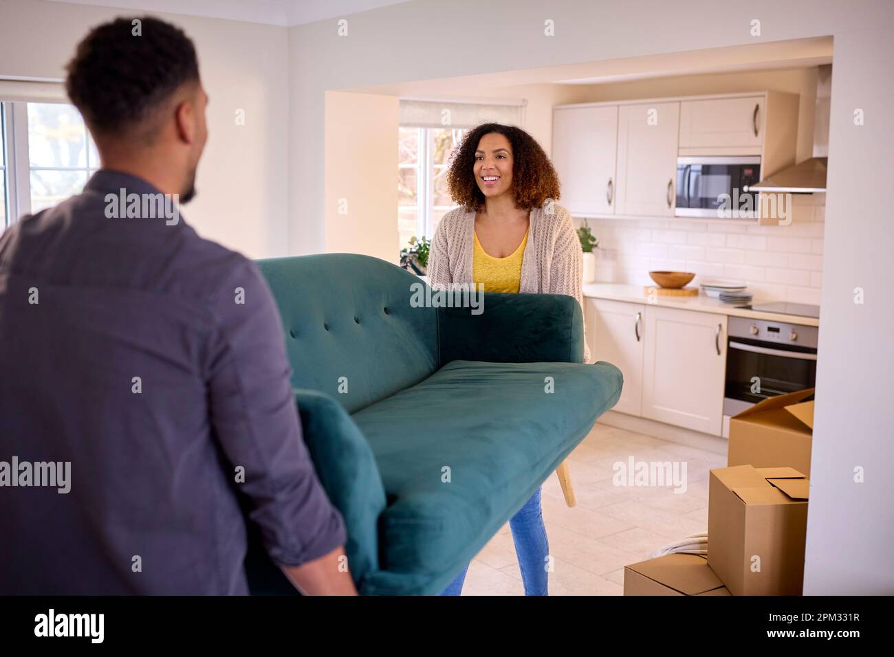 Couple Unpacking Boxes And Carrying Sofa Into New Home On Moving Day ...