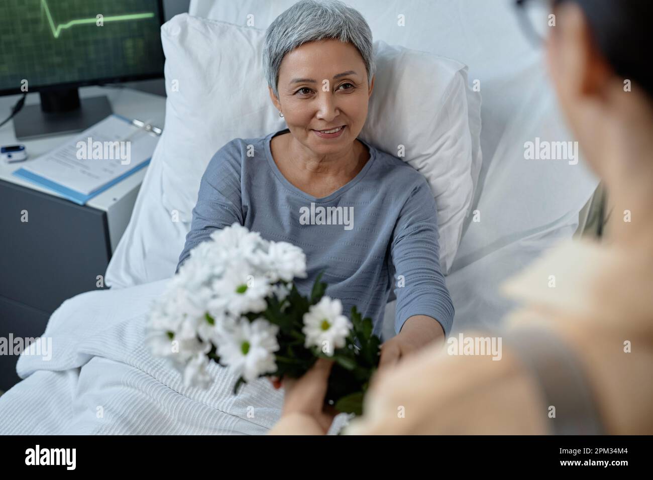 Senior sick woman getting flowers from her daughter during her visit in