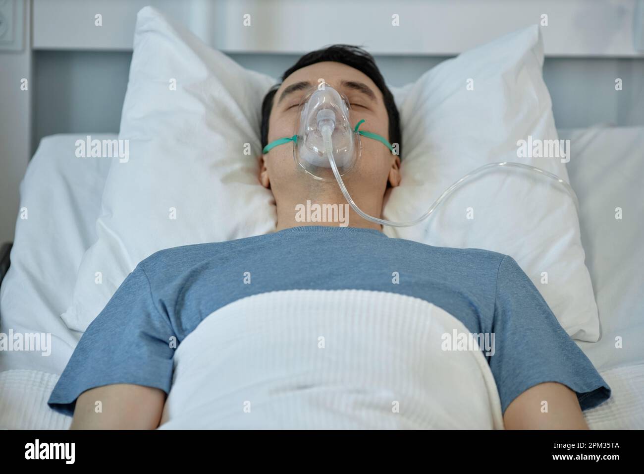 Young man in oxygen mask on his face lying on bed during rehabilitation