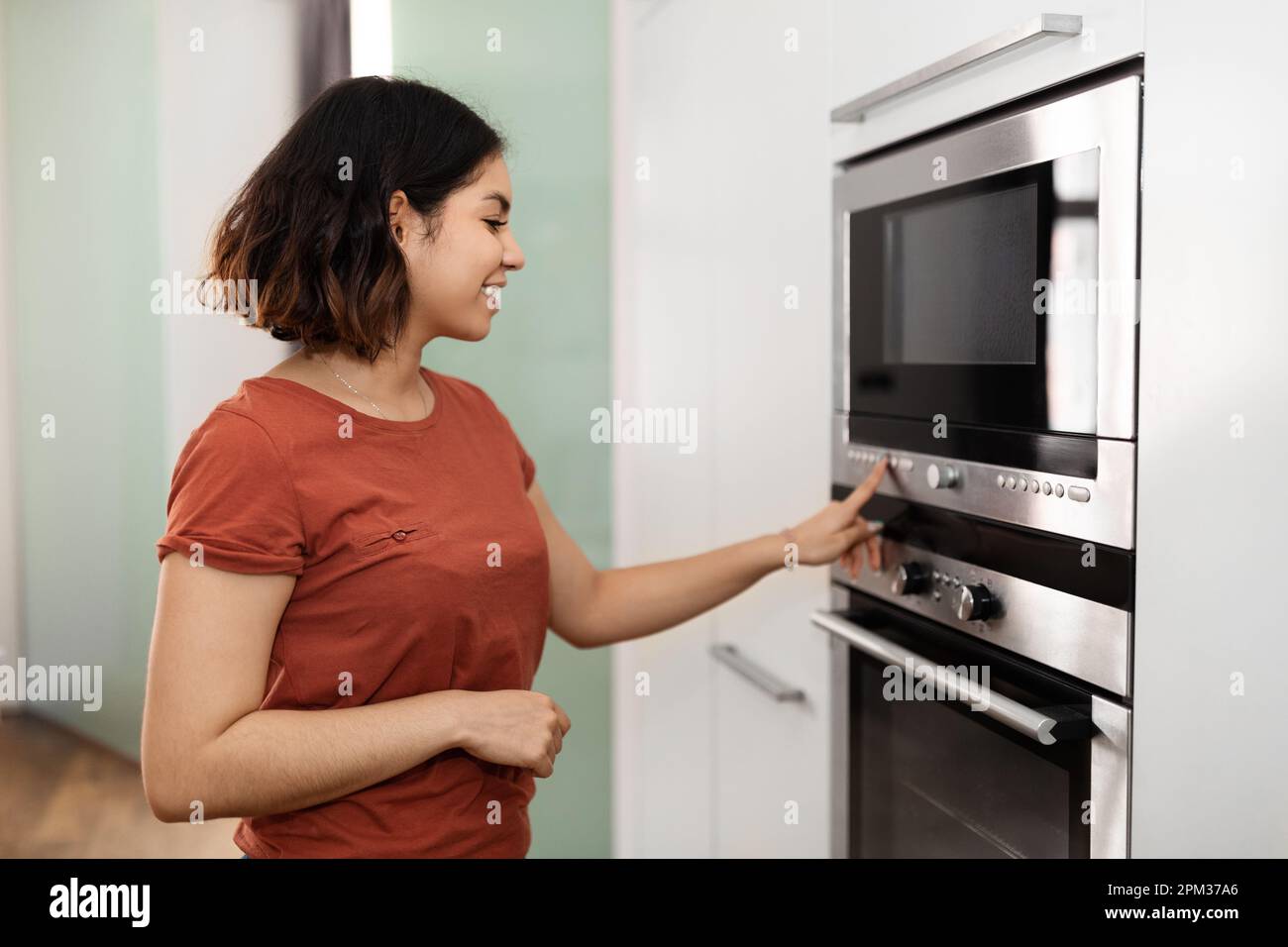 Beautiful arab female turning on electric oven in kitchen Stock Photo