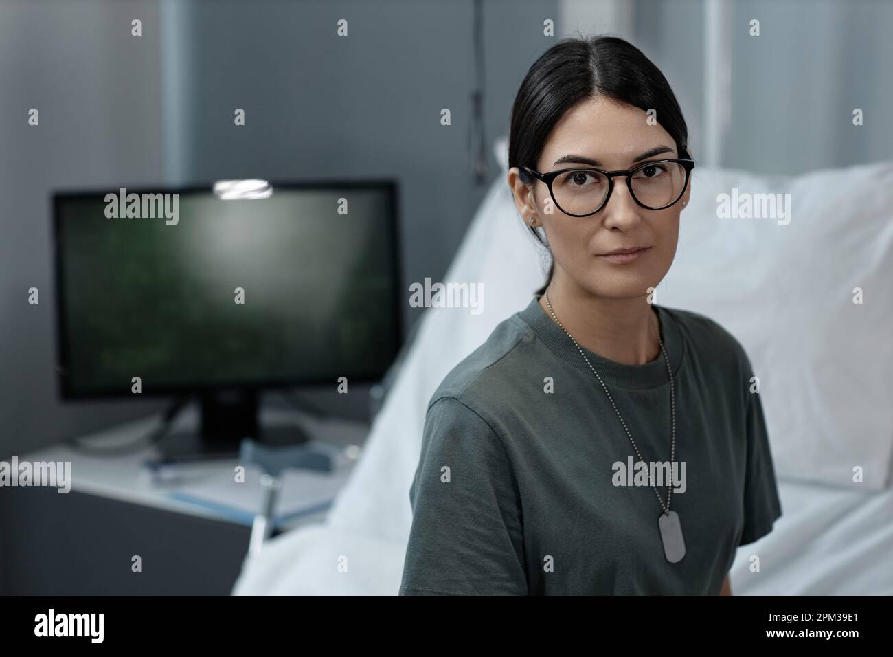 Portrait of female soldier in eyeglasses looking at camera sitting in