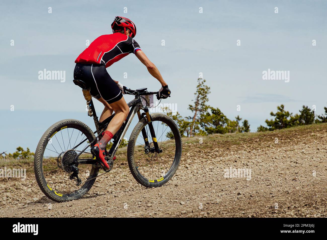 cross-country cycling, athlete cyclist riding mountain bike uphill on gravel road Stock Photo