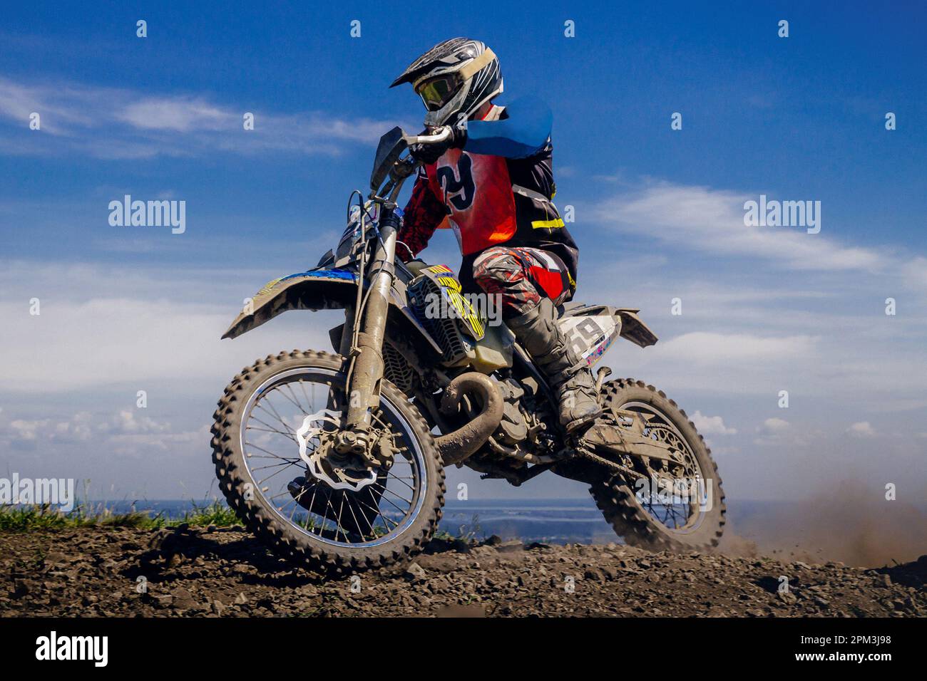 close-up motocross rider riding off-road motorcycle racing dusty trail on background blue sky Stock Photo