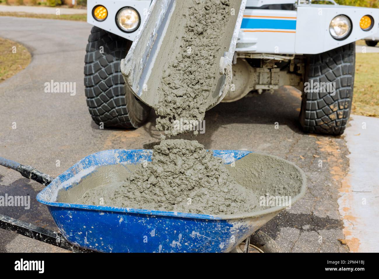 Mixer truck pours concrete into wheelbarrow at construction site Stock