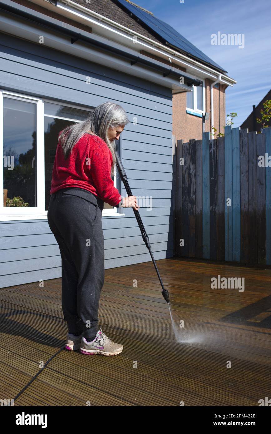 Woman cleaning timber deck with a pressure washer Stock Photo