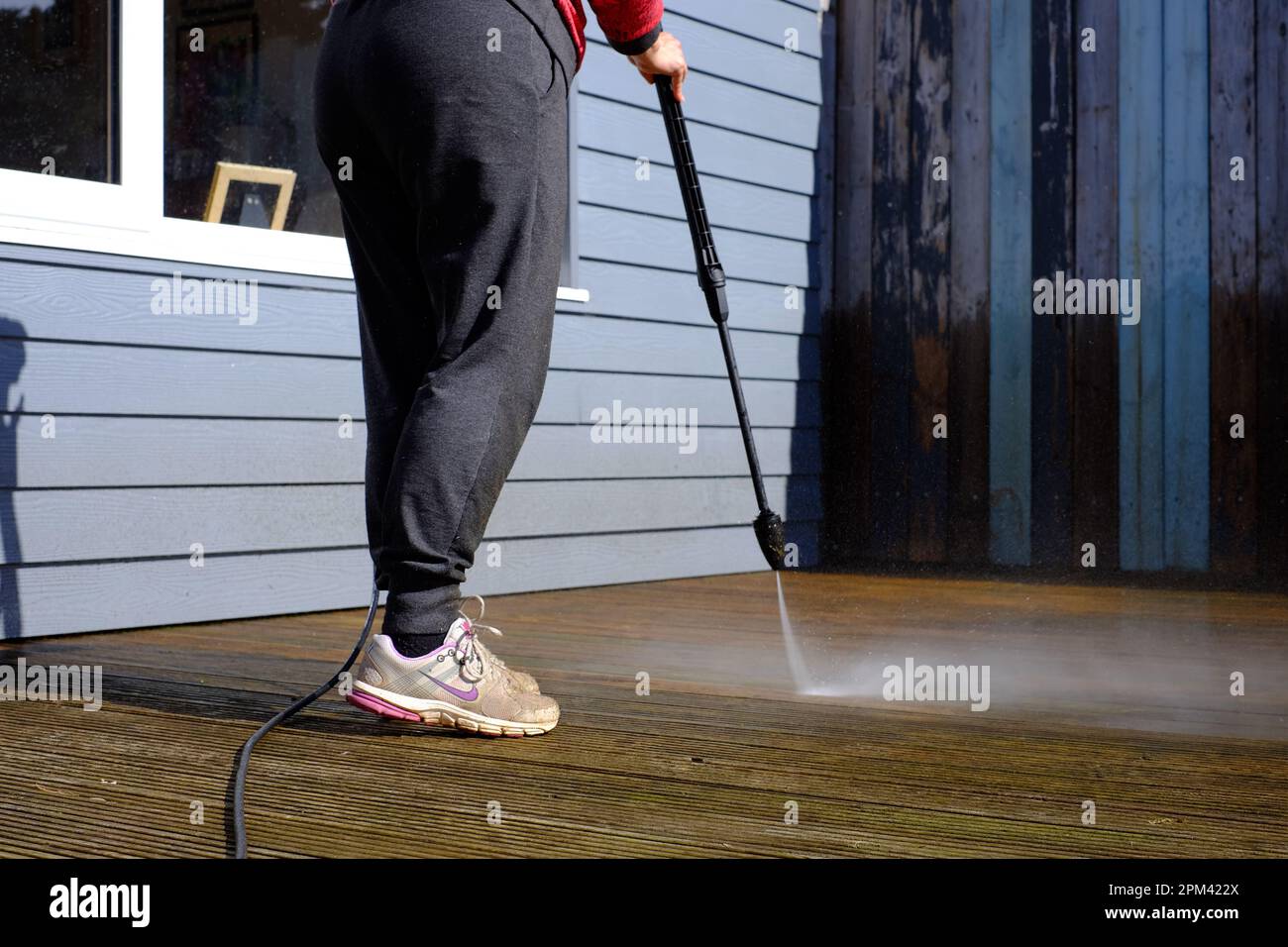 Woman cleaning timber deck with a pressure washer Stock Photo