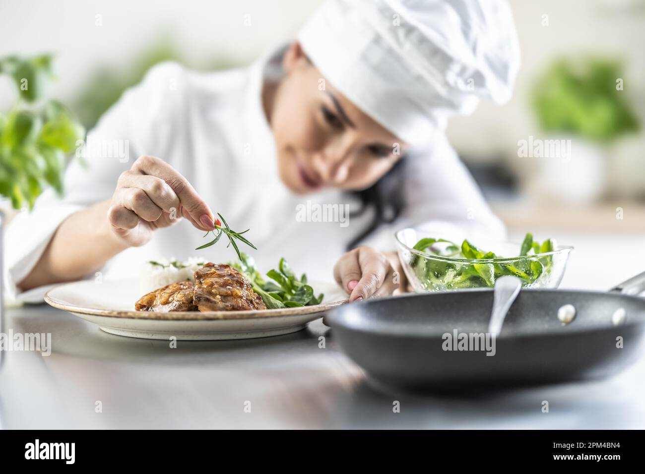 A young female chef finishes a meal with a sprig of rosemary in a