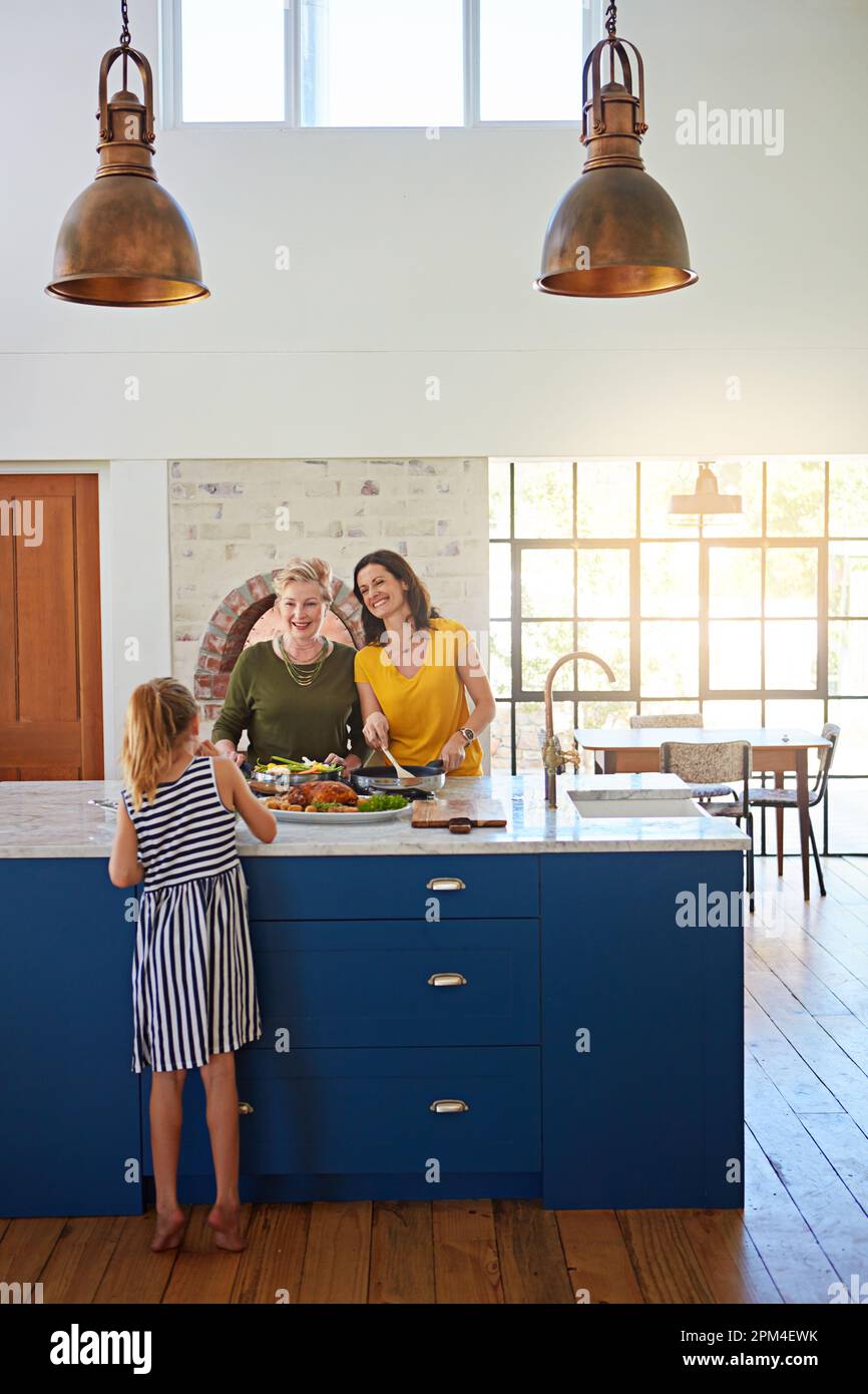 Food brings everyone together. a little girl in the kitchen while her mother and grandmother prepares supper. Stock Photo