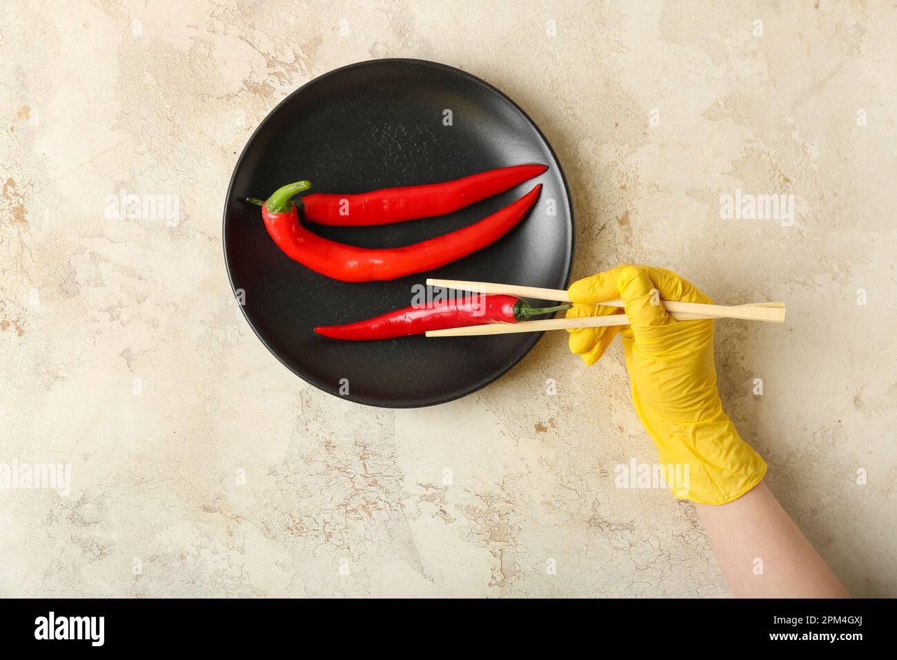 Woman in rubber glove with chopsticks and plate of chili peppers on grunge background Stock Photo