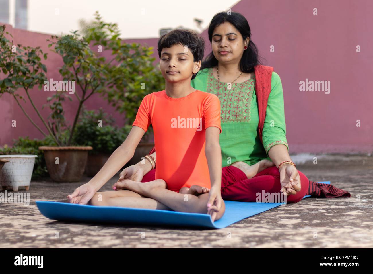 An Indian girl child with mother practicing padmasana yoga on yoga mat ...