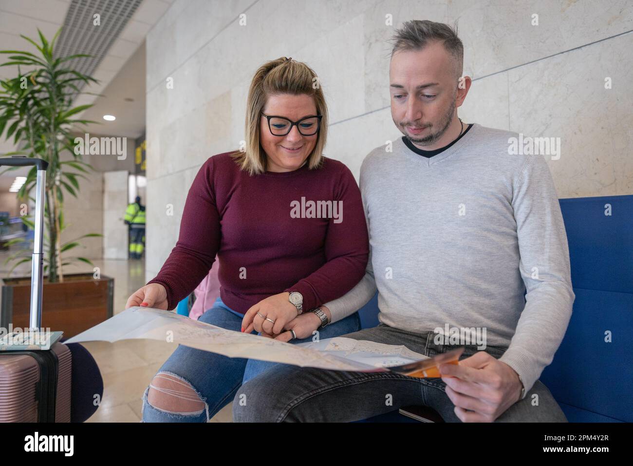 A couple of tourists look at the map at the airport with suitcases Stock Photo