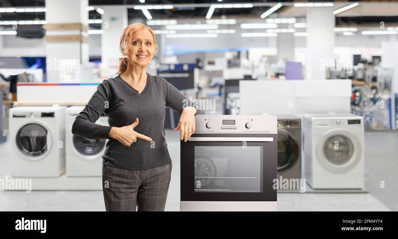 Happy mature woman pointing at an oven inside a home applances store Stock Photo