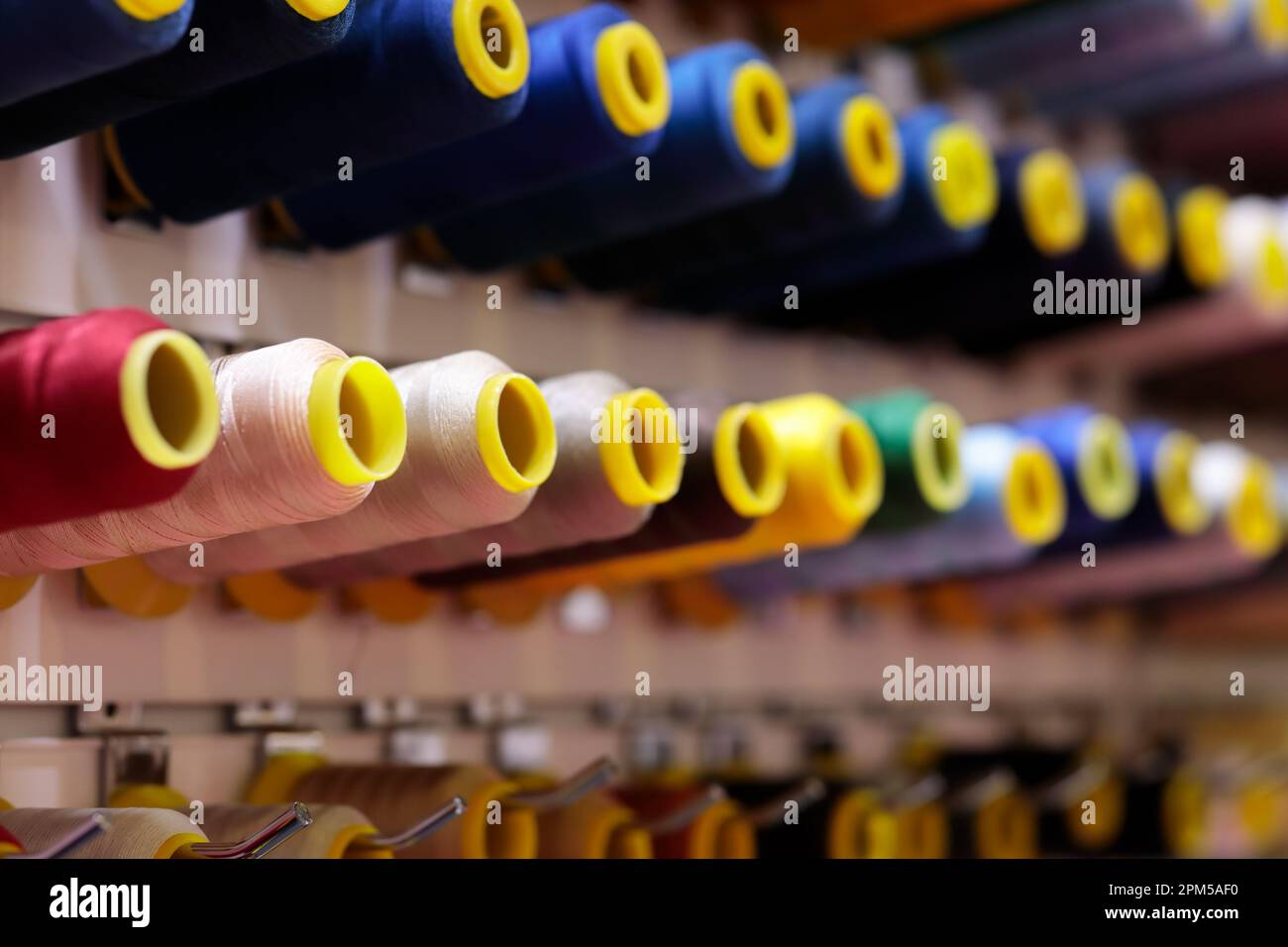 Multicolored sewing threads bobbins on stand in a shop. Selective focus. Stock Photo
