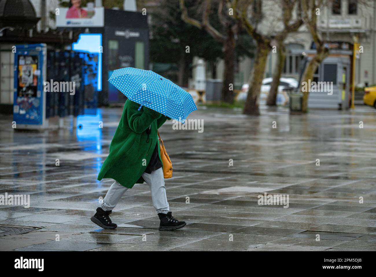 A woman holds an umbrella to protect herself from the heavy rainfall. Heavy rain in Istanbul negatively affected life in Kadikoy. People were seen walking with umbrellas to protect themselves from the rain. Stock Photo