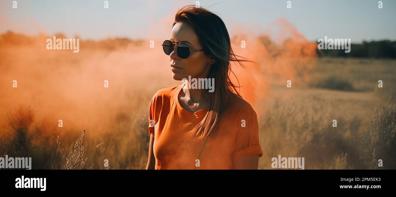 woman standing in open field surrounded by orange smoke Stock Photo