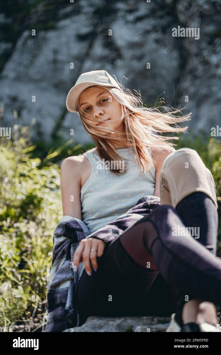 a girl in a gray top and a white cap sits on a stone Stock Photo