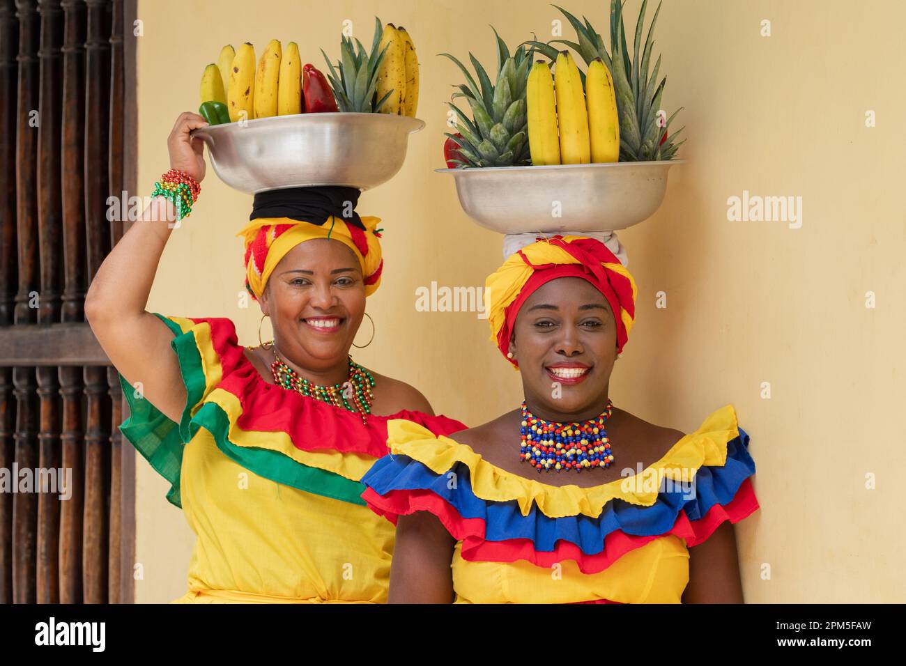 Happy smiling Palenquera fresh fruit street vendors in the Old Town of Cartagena, Colombia. Cheerful Afro-Colombian women in traditional costumes. Stock Photo