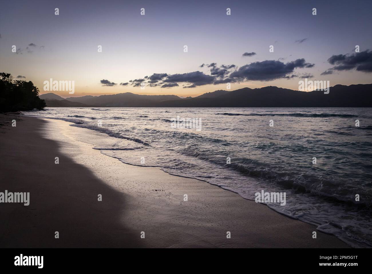 Carribean beach and waves at sunset with mountains in distance Stock Photo