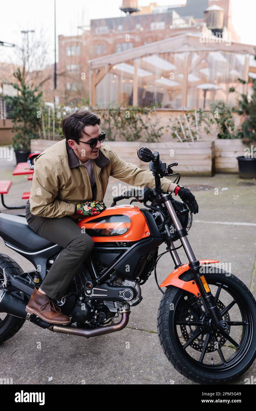 Man on orange and black motorcycle parked in outdoor courtyard Stock Photo