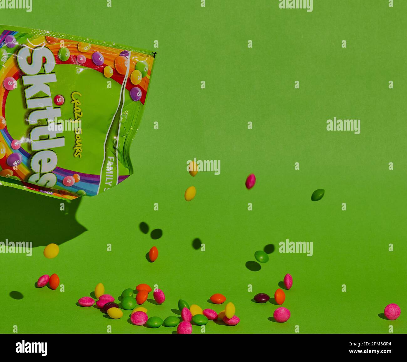 Packet of opened Skittles sweets with Skittles falling out of them shot