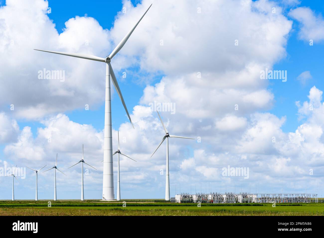 Wind park with tall wind turbines and an electricity substation under blue sky with clouds in summer Stock Photo