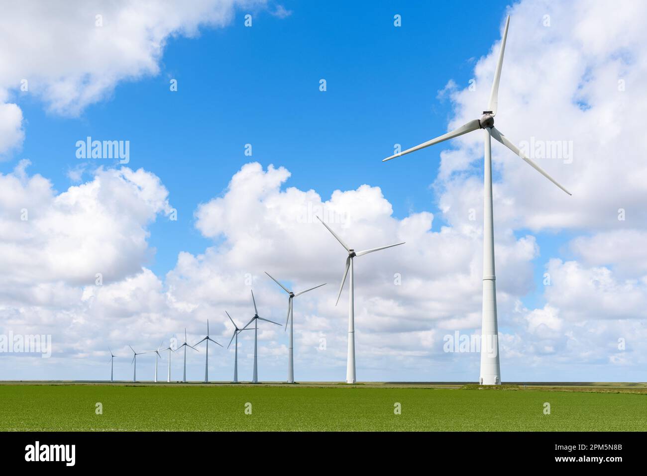 Row of wind turbines under blue sky with clouds in summer Stock Photo