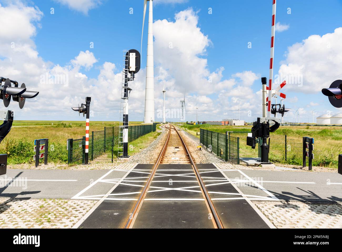 Level crossing along a railway to a commercial port on a sunny summer day. Wind turbines line the tracks. Stock Photo