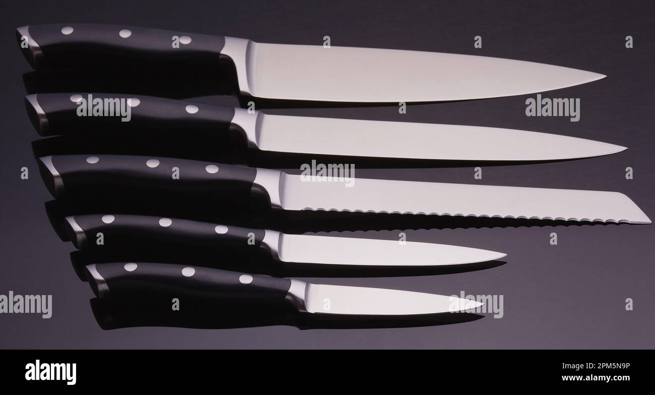 Full set of chefs knifes on a black background with a gradient over the blades. Stock Photo