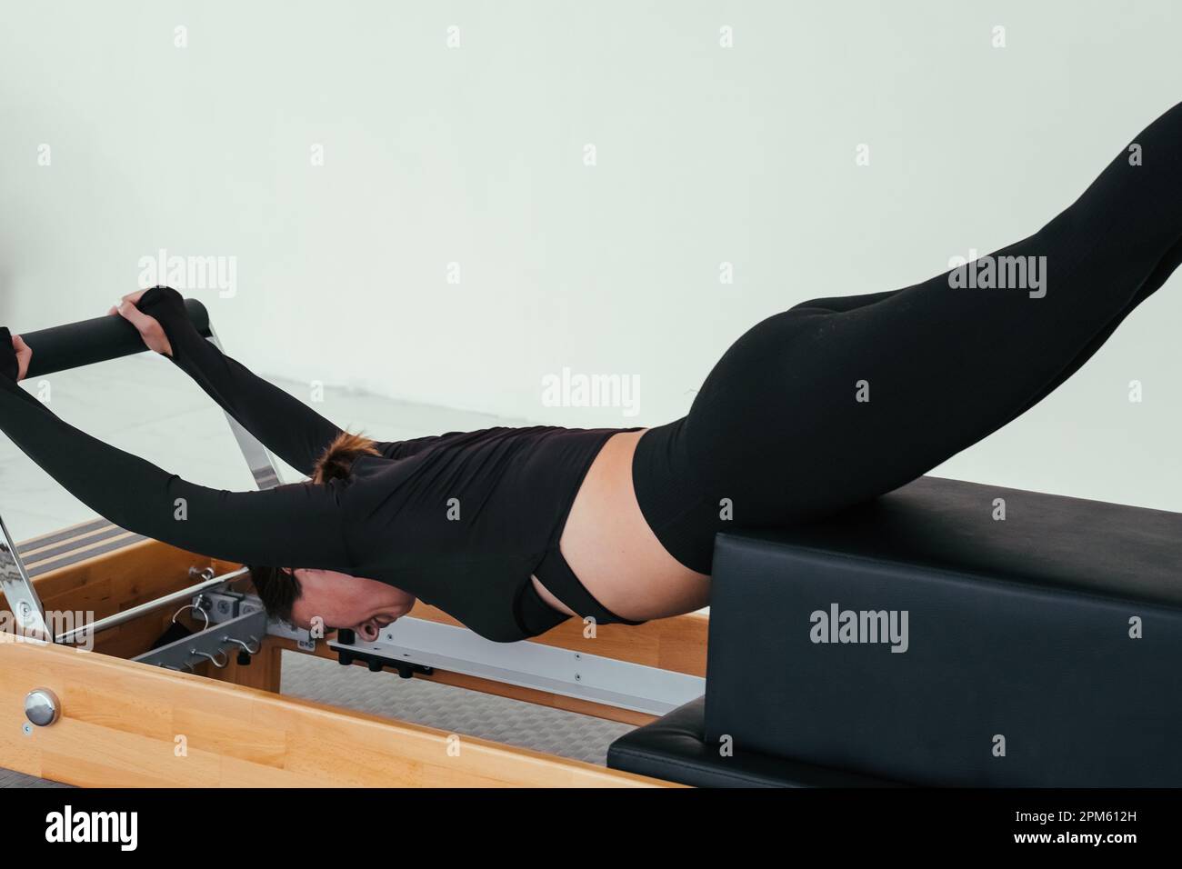 Woman doing Pilates on reformer bed. Pilates reformer, girl doing backbends. Stock Photo