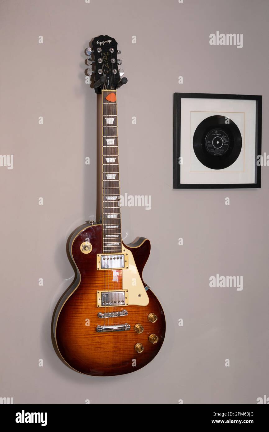 A classic Les Paul Epiphone Standard electric guitar hanging on a wall next to a framed vinyl record of You'll Never Walk Alone, UK Stock Photo