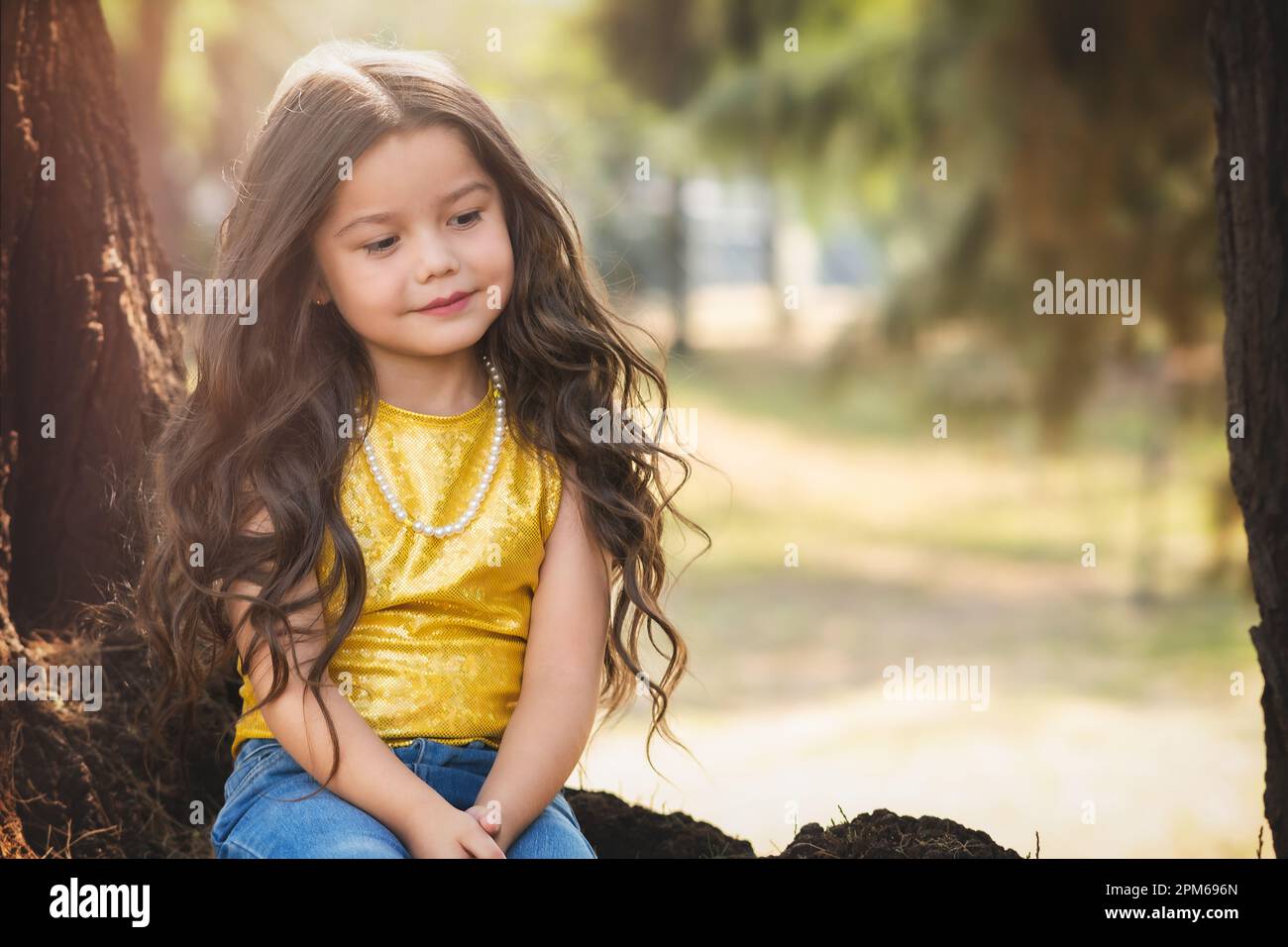 Blonde preschool girl sitting in a tree has a happy time in nature, cute smile. children's day theme. Stock Photo