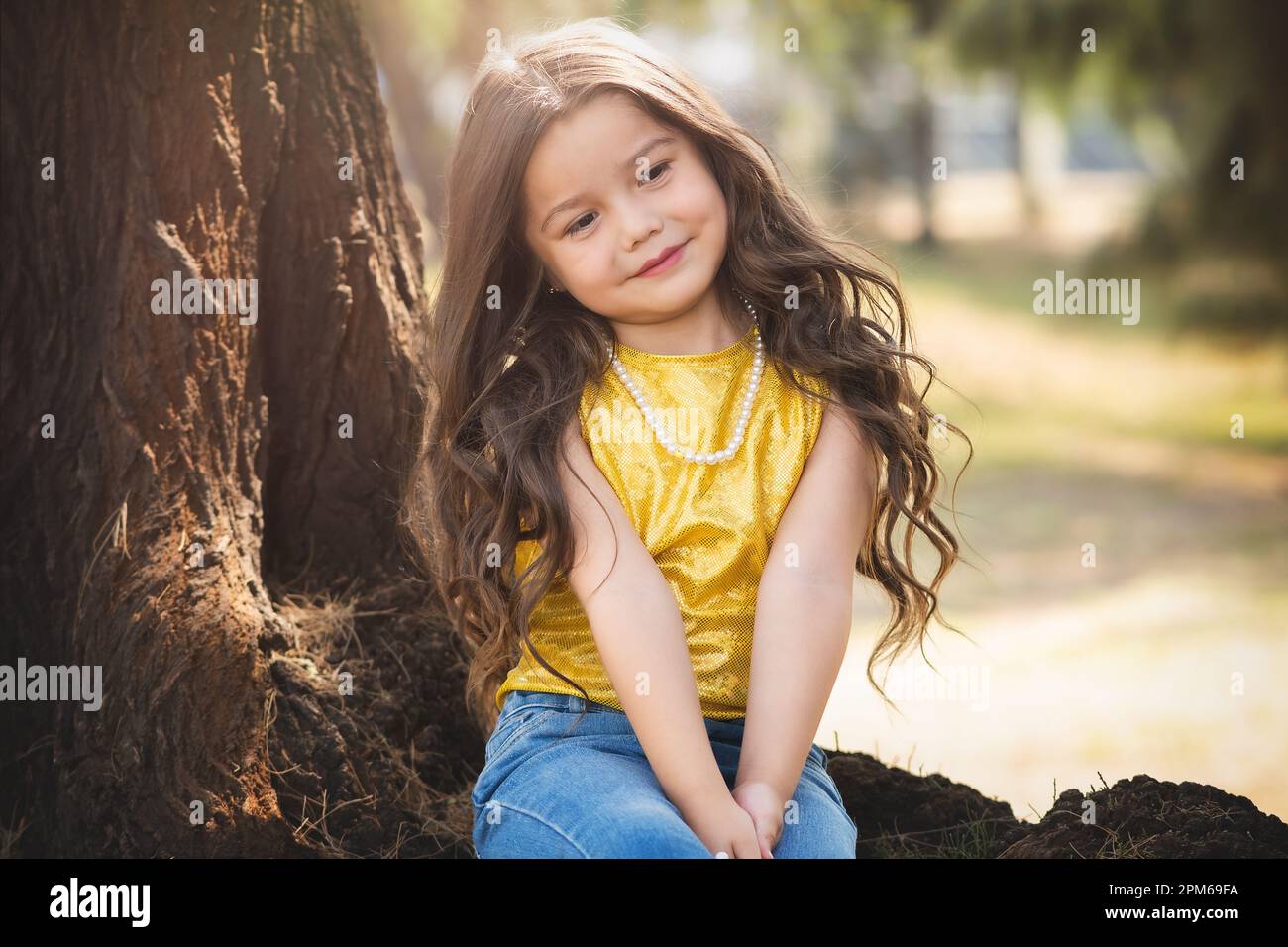 Blonde preschool girl sitting in a tree has a happy time in nature, cute smile. children's day theme. Stock Photo