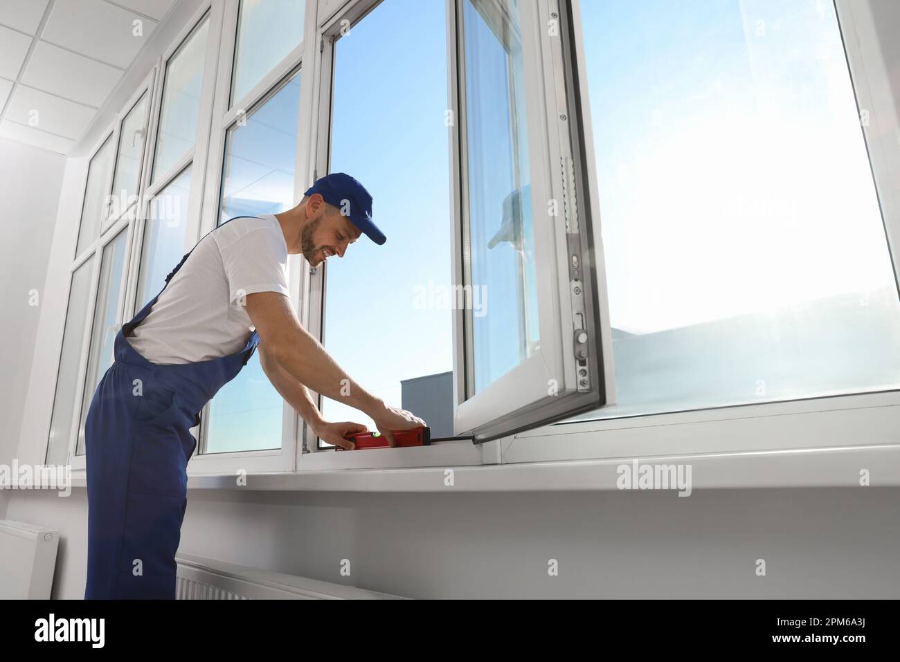 Worker using bubble level after plastic window installation indoors Stock Photo