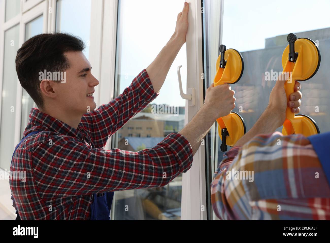 Workers using suction lifters during plastic window installation indoors Stock Photo